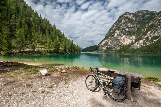 A bicycle leaned against a wooden chair near a beautiful lake surrounded by trees