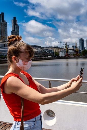 A vertical shot of a Hispanic female with a face mask taking a selfie outdoors - concept of the new normal