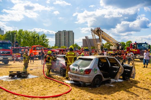 Firemen killing a fire in a damaged Peugeot car with open doors during a fire department event.