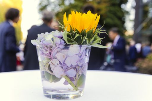 A selective focus shot of colorful flowers in a cup with blurred people in the background