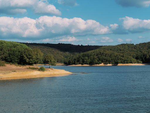 A beautiful shot of a lake surrounded by hill forests and sand beach during a cloudy weather