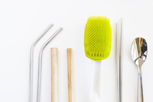A top view of a bamboo and metal straw, spoon, chopsticks and brush on the white background