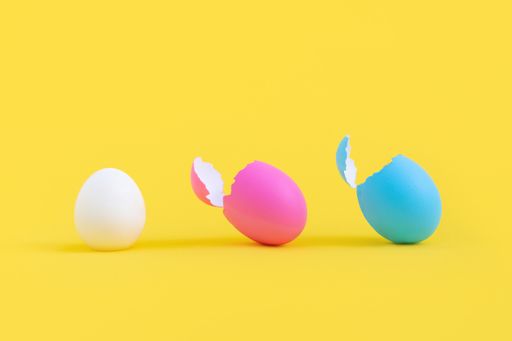 A closeup shot of pink and blue eggshells with a peeled egg isolated on the yellow background in a row