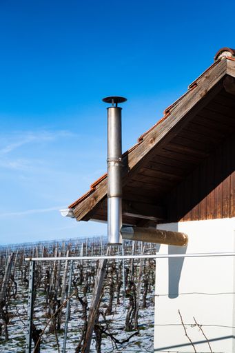 A vertical shot of a chimney of a small wooden hut in a snowy vineyard