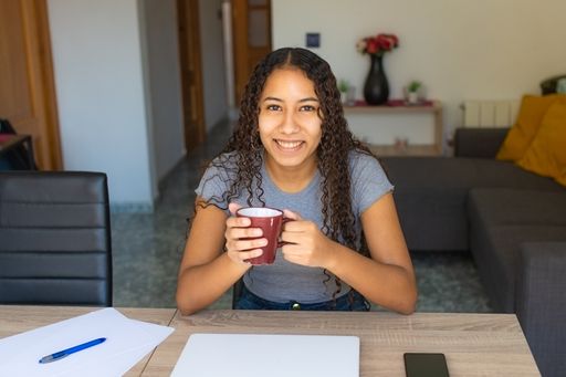 A young Latin female smiling and drinking a coffee while studying