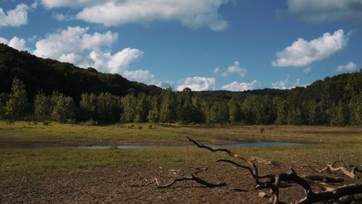 A beautiful shot of a water stream that goes through a grass field surrounded by hill forests