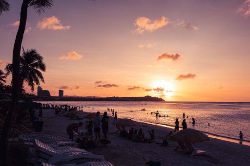 A tranquil beach scene at dusk, with a beautiful orange and pink sky and silhouettes of people