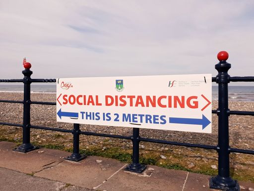 Social distancing sign with an indication of 2 metres distance. The sign on the fence in Bray Seafront, Ireland. The Irish Sea in the background.