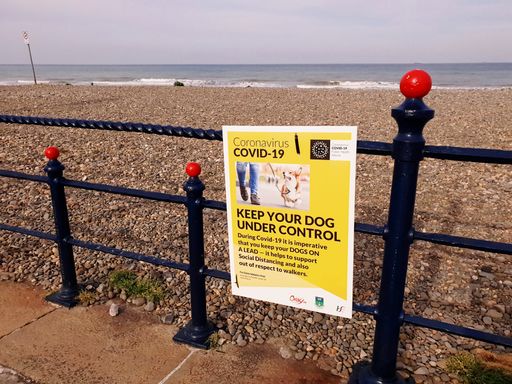 Sign with the message for dog owners to support social distancing during the COVID-19 outbreak in Ireland. The Irish Sea in the background.