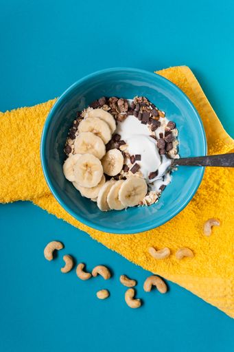 An overhead shot of a blue bowl full of cereal and banana on a yellow rag