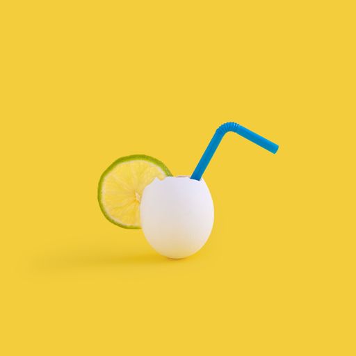 A closeup shot of an eggshell with a slice of lime and cocktail tube isolated on the yellow background