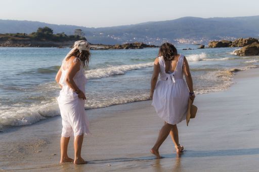 Two ladies wearing matching white summer dress walking on the sandy beach
