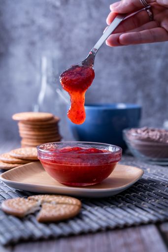 A vertical shot of a hand holding a spoon of strawberry jam