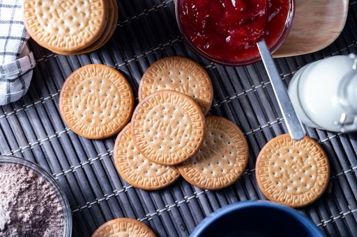 A top view of fresh Maria cookies (galletas Maria), strawberry jam, cocoa powder, milk, and a bowl
