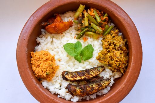 A top view shot of a brown ceramic bowl with rice, mint in the middle of it, curry, cooked fish, and salads on a white surface