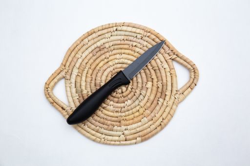 A top view of a black matte sharp kitchen knife on a straw chopping board isolated on white