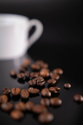 A vertical shot of a heap of roasted coffee beans with a cup in the background