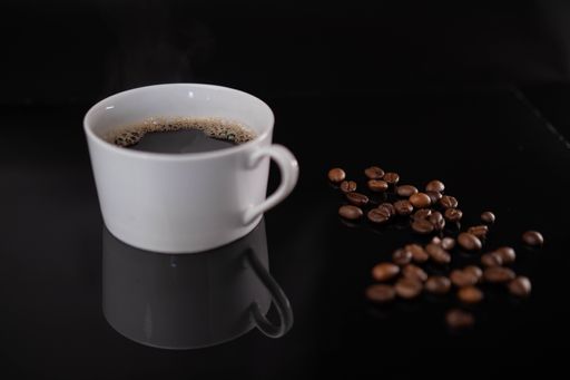 A cup of espresso and roasted coffee beans on a black background
