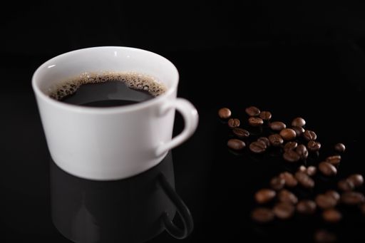 A cup of espresso and roasted coffee beans on a black background