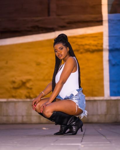 An African-American female model with braids posing in a street in shorts and high boots