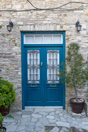 A blue modern door on an old building in Lefkara, Cyprus with lamps and plants in front of it