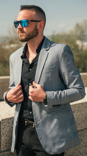 A vertical shot of a handsome Hispanic male with gray suit and glasses outdoors