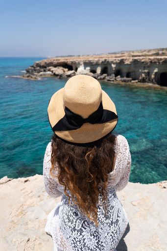A vertical back view of a tourist female in a hat sitting near the sea