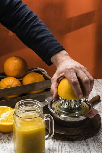 A person making fresh orange juice with oranges in the background