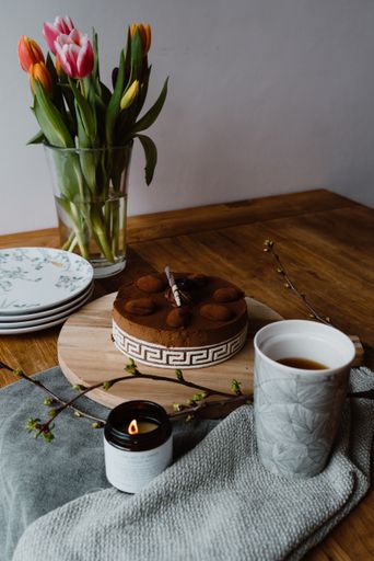 A vertical shot of tulips in a vase, a cup of espresso and a delicious chocolate cake on a table