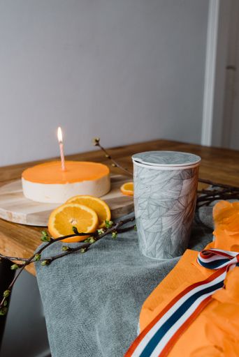 A vertical shot of a lighting candle, delicious fruit cake and a cup of hot espresso on a table