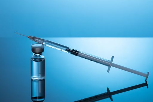 A closeup shot of a covid19 vaccine bottle with a needle on a blue background - covid19 concept