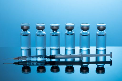 A closeup shot of covid19 vaccine bottles with a needle on a blue background - covid19 concept