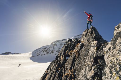 Climber or alpinist at the top of a mountain. Success of mountaineer reaching the summit. Outdoor adventure sports in winter alpine moutain landscape