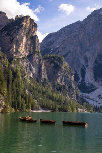A vertical shot of the Fanes-Sennes-Braies Nature Park - a line of small boats on calm water with tall mountains and thick trees
