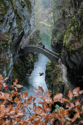 A vertical shot of a person looking over a stone bridge surrounded by mossy cliffs