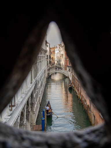 A vertical shot of a river in Venice shown through a keyhole, with classical buildings and bridges