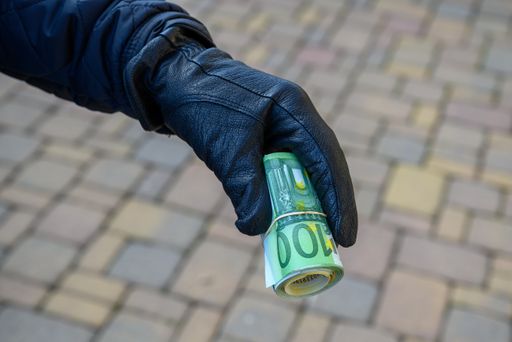 A selective focus shot of a hand wearing a leather glove holding a roll of euro banknotes