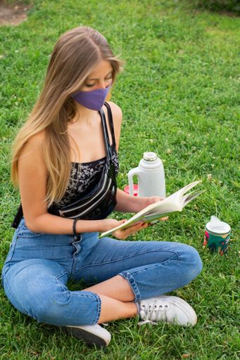young and attractive woman reading a book in a natural space, sitting with an Argentine mate next to it with its respective mask