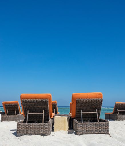 A vertical shot of straw deck chairs with orange pillows in the beach during the daytime