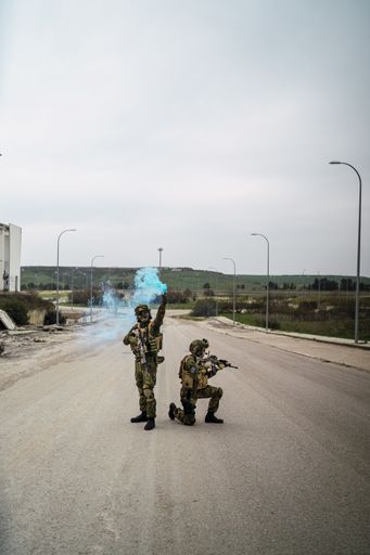 A vertical shot of an armed special force soldier holding a blue smoke bomb during the investigation