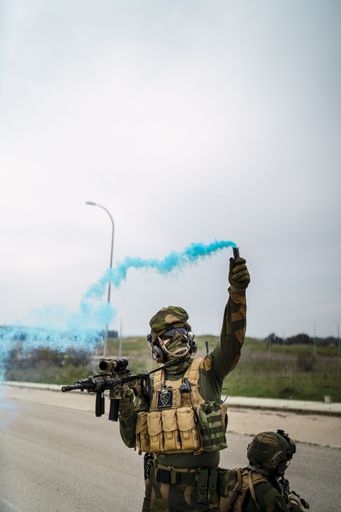 A shallow focus of an armed special force soldier holding a blue smoke bomb during the investigation