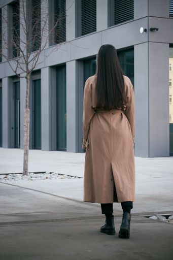 A vertical shot of a brunette wearing a coat, black pants, and boots walking in a snowy street