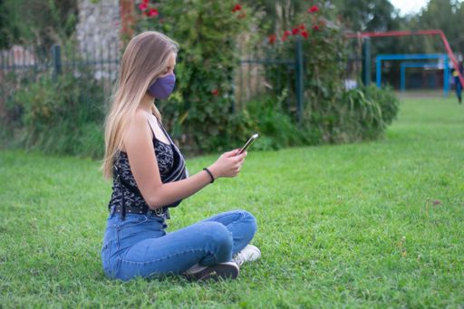 A closeup shot of a Caucasian model sitting on a grassy ground with her phone