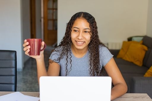 A young girl smiling with a cup of coffee at the lounge table while she's working online