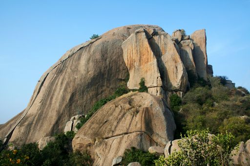 A closeup shot of the huge rock surrounded by trees in the blue sky background