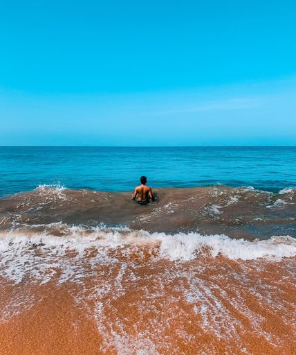 A vertical back view of a shirtless man walking into wavy seawater
