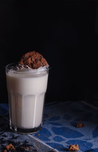 A vertical shot of chocolate cookie dropping in a glass of milk
