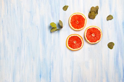 A top view of fresh grapefruit slices and dry leaves isolated on the white-blue background