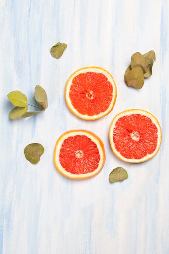 A vertical shot of fresh grapefruit slices and dry leaves isolated on the white-blue background