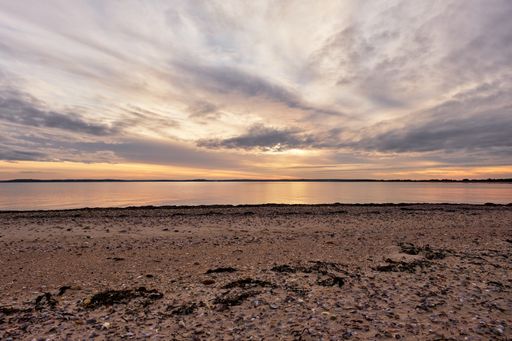 A beautiful shot of a calm ocean with a scenery of sunset in a cloudy blue sky